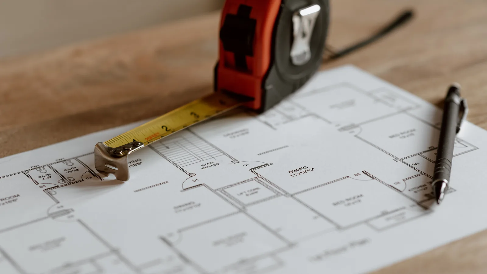 A tape measure and a pen resting on a printed floor plan of a home