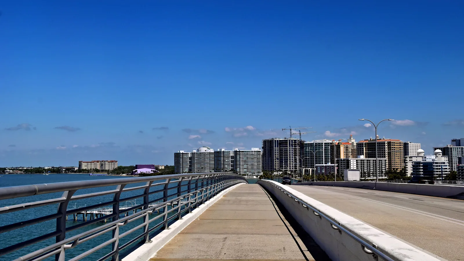 A causeway walkway over open water, with a line of bayfront towers along the shore ahead