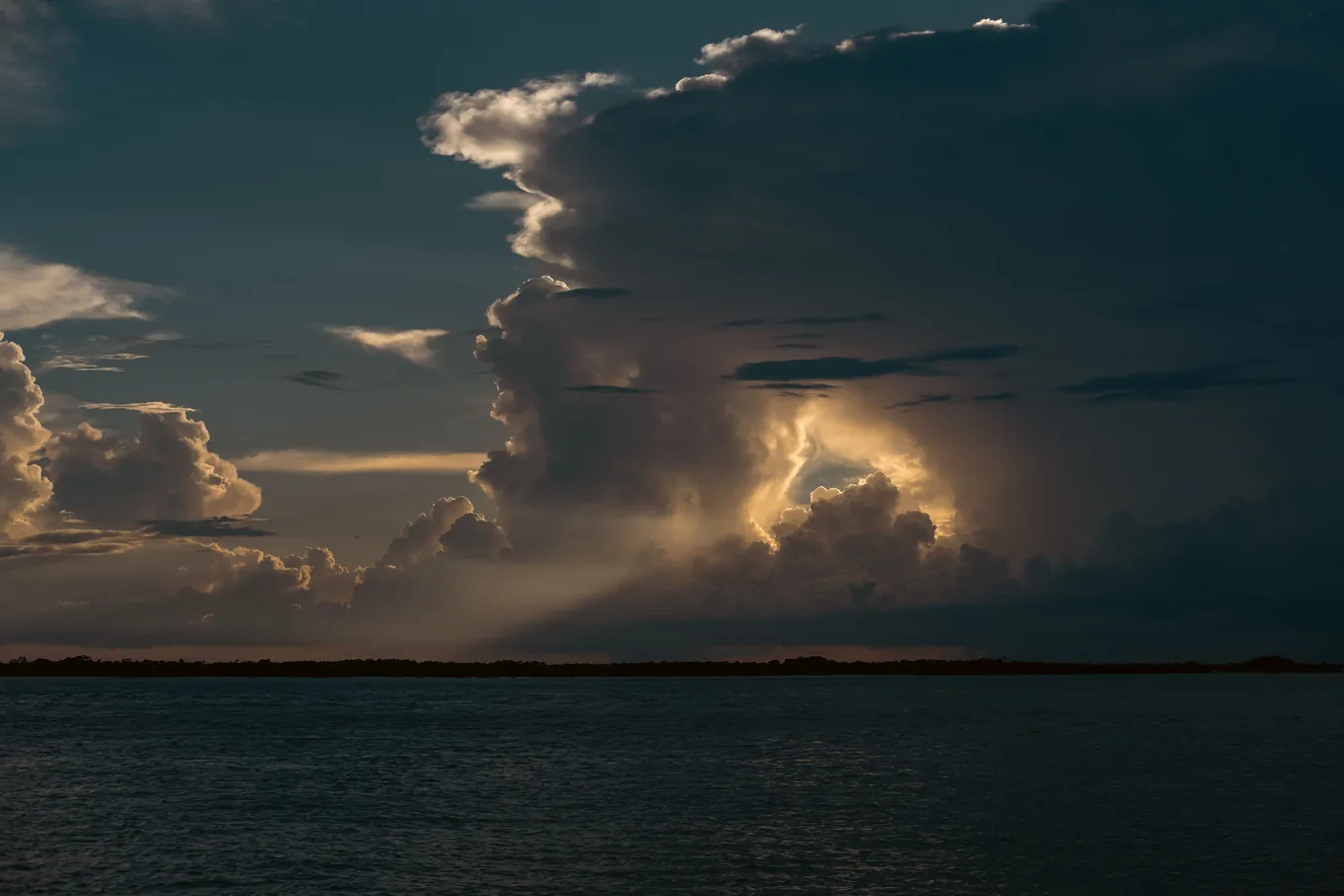 Tall storm clouds building over open water in the late afternoon, seen from the shoreline