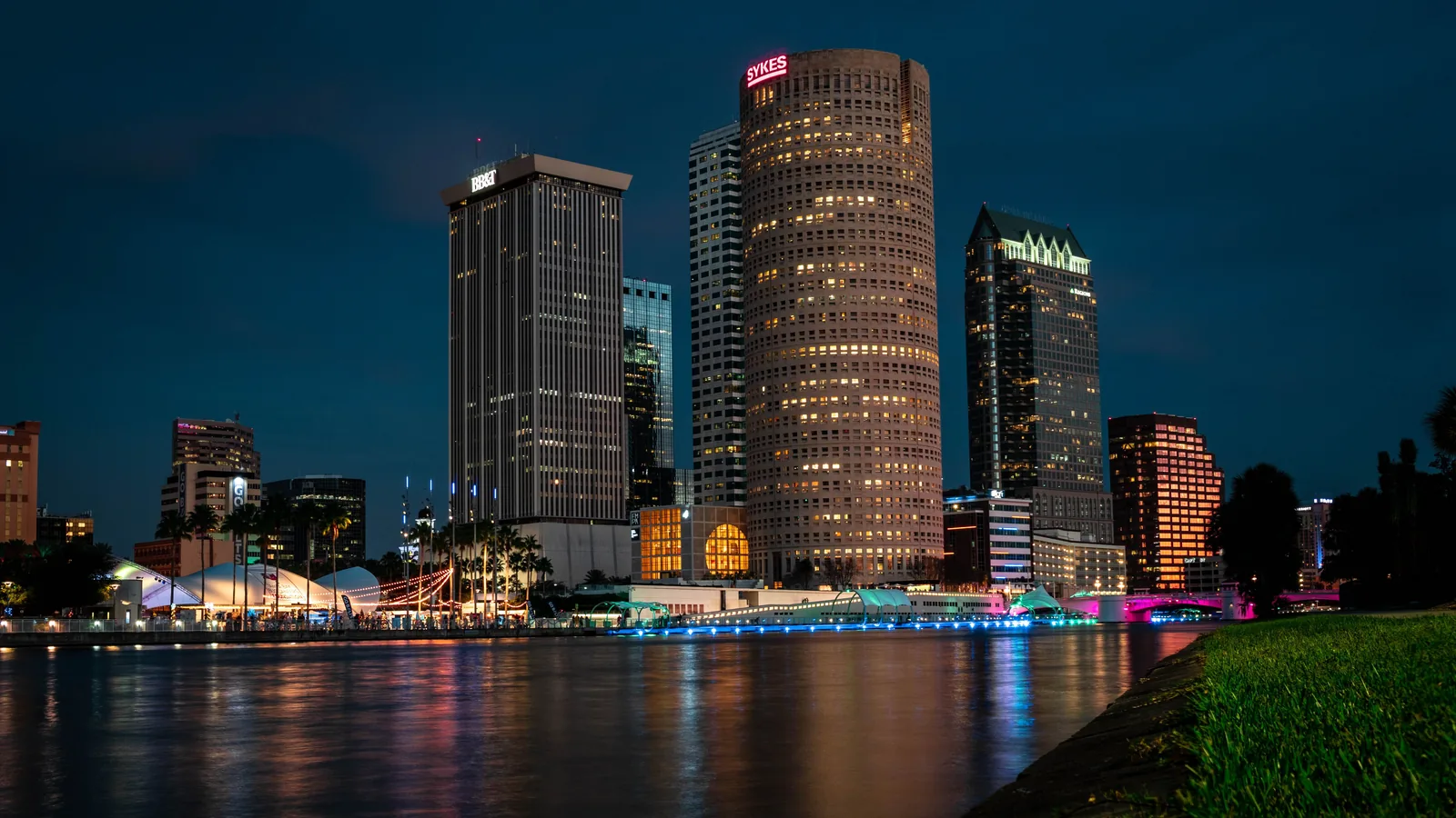 Downtown Tampa&rsquo;s towers lit at night across the Hillsborough River, with the Riverwalk along the water