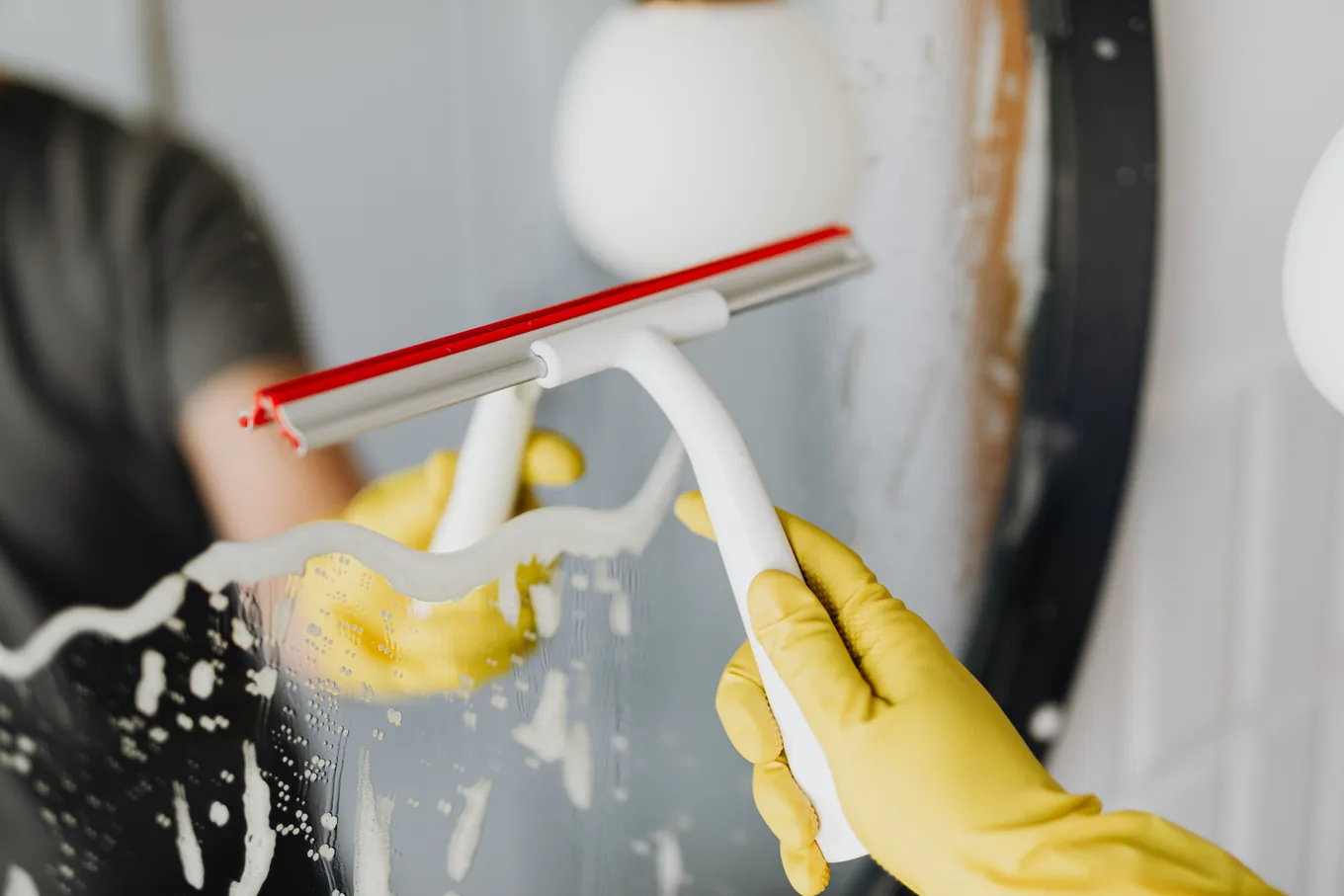 Gloved hands pulling a squeegee across soapy glass, leaving a clean strip behind the blade