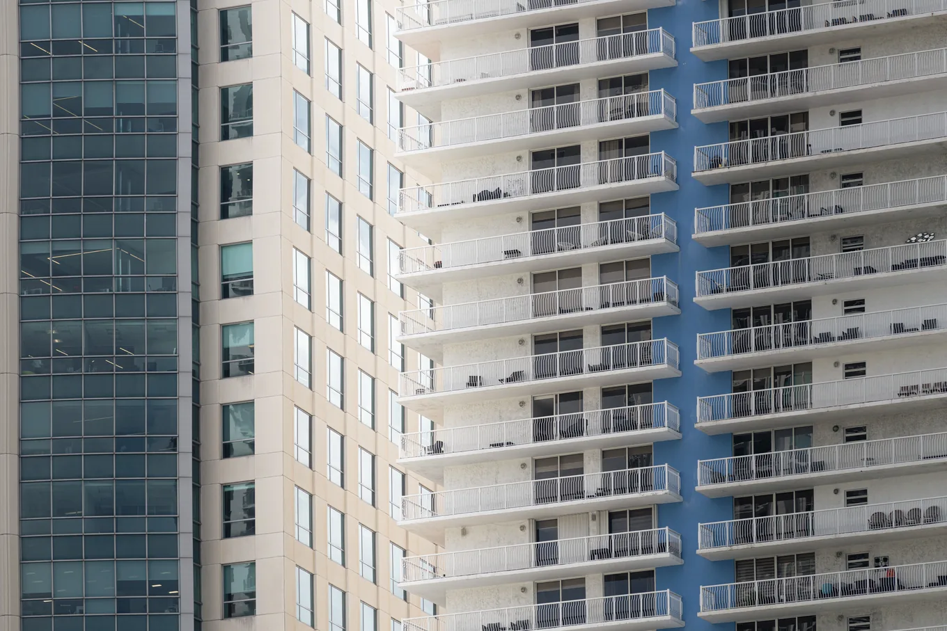 Rows of balconies with white railings stacked up a residential tower in Miami, beside a glass office building