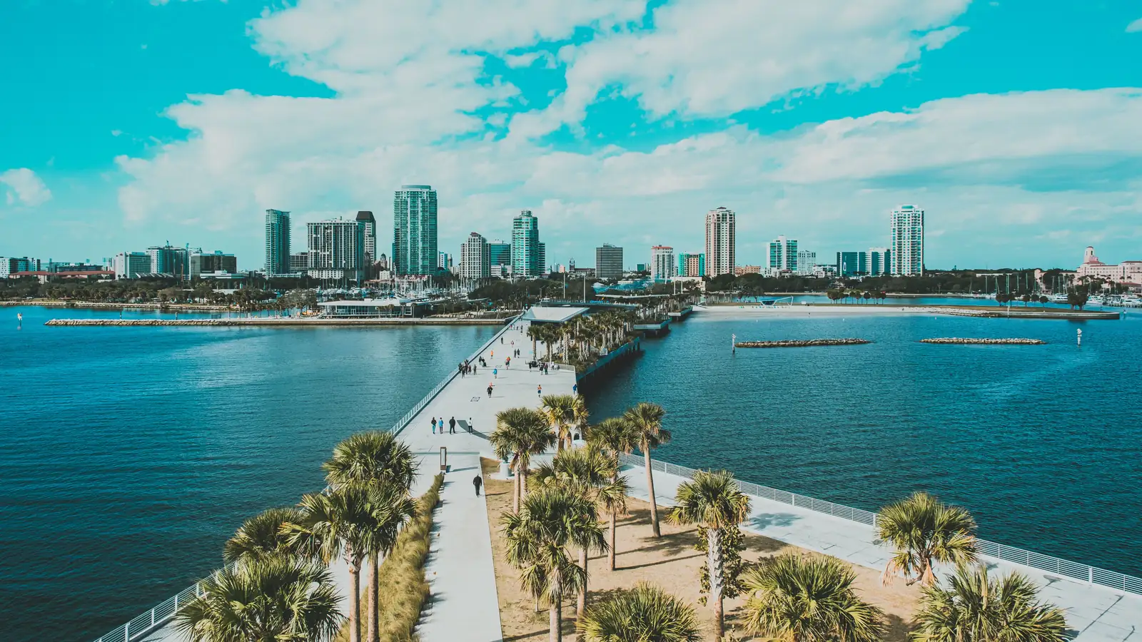 Downtown St. Petersburg&rsquo;s waterfront high-rises seen from the St. Pete Pier, with palm trees and Tampa Bay in front