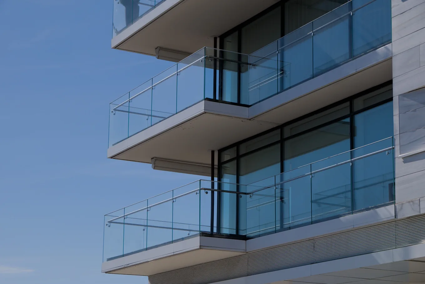 Stacked concrete balconies with frameless glass panels and a thin metal top rail on a modern tower