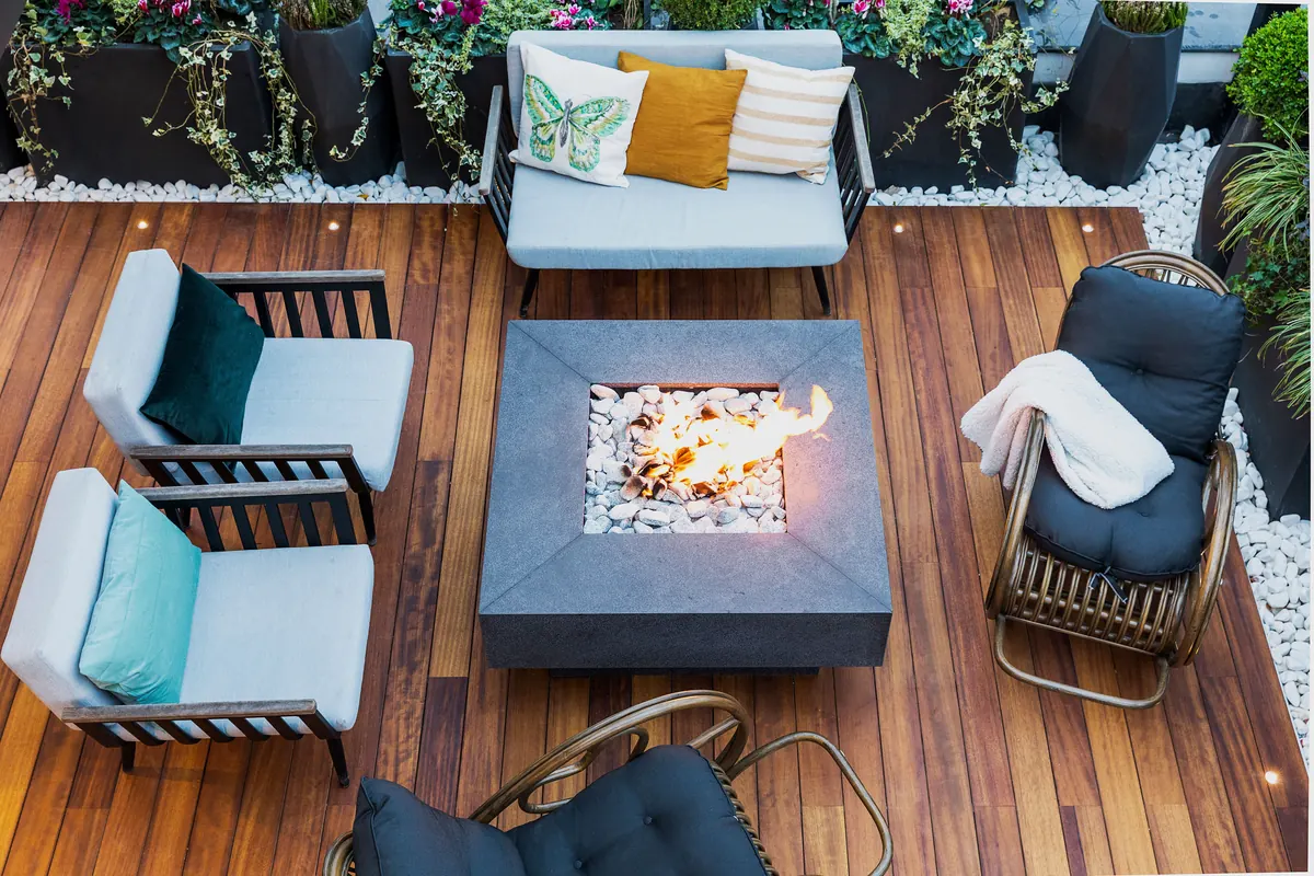 Overhead view of a wood deck with cushioned chairs, a loveseat with patterned pillows and a square fire table
